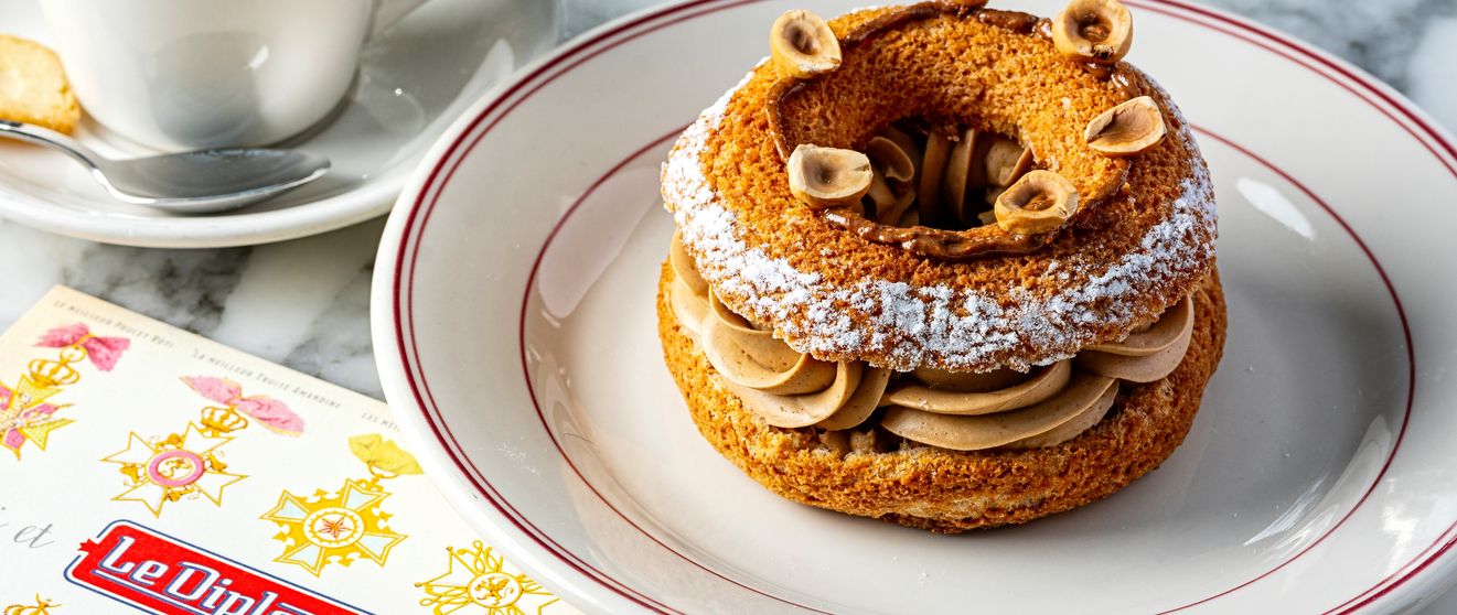 A gourmet dessert with layers of pastry and cream, topped with powdered sugar and hazelnuts, accompanied by a cup of coffee on a marble table.