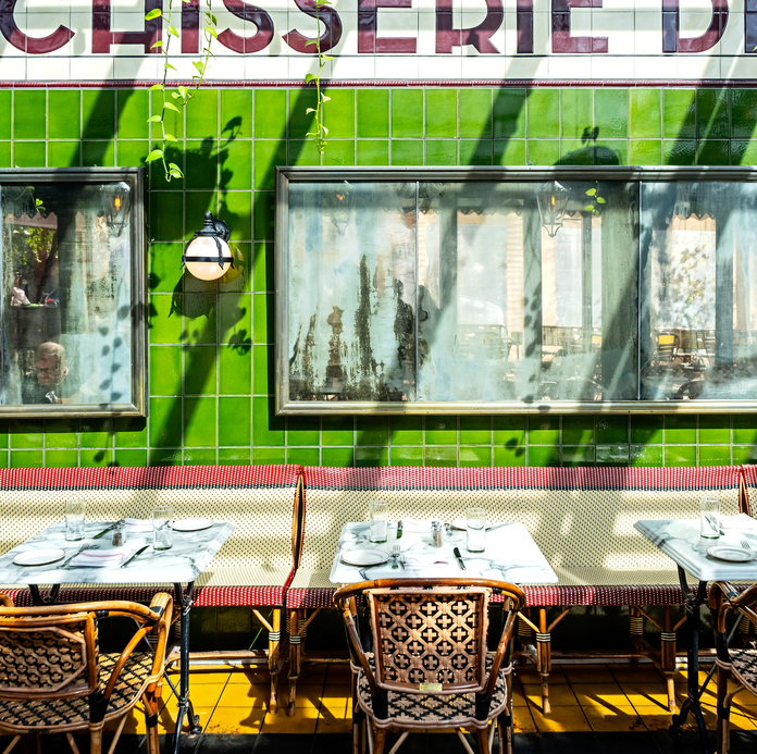 A chisserie restaurant with green tiled walls, outdoor tables with wicker chairs, a menu board, and star-patterned floor tiles.