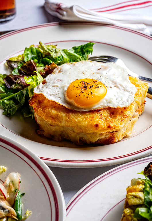 Golden hash brown casserole topped with a sunny-side-up egg served with a side salad on a white plate with red trim.